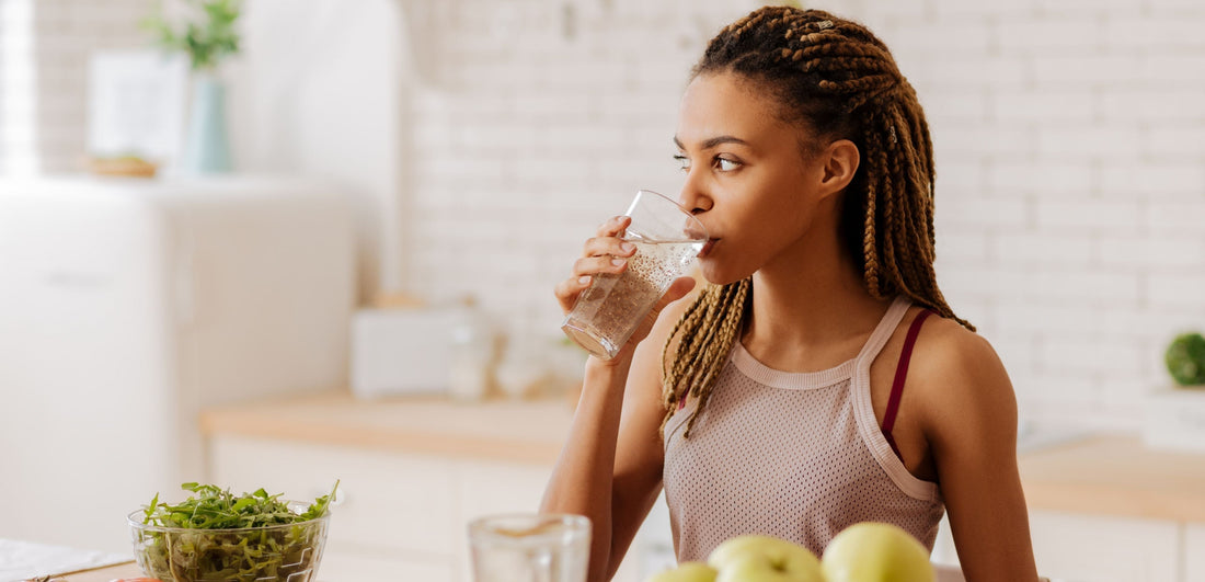 Woman drinking water in a kitchen with fruits on the counter