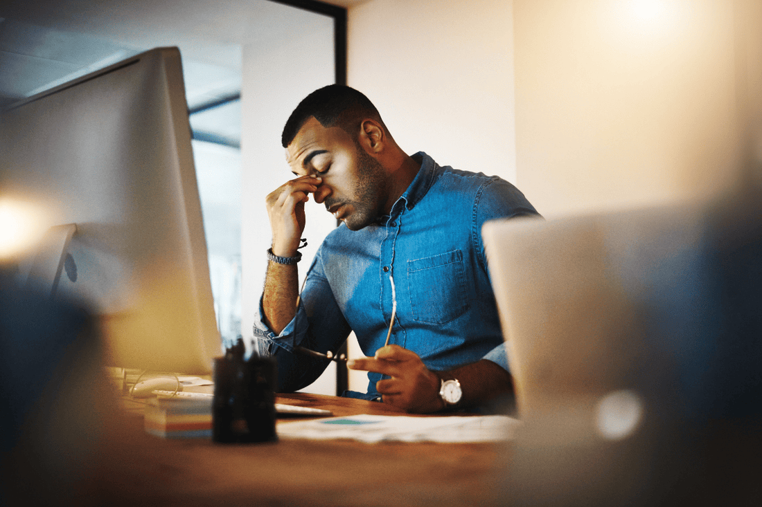 man stressed and rubbing his head at work desk