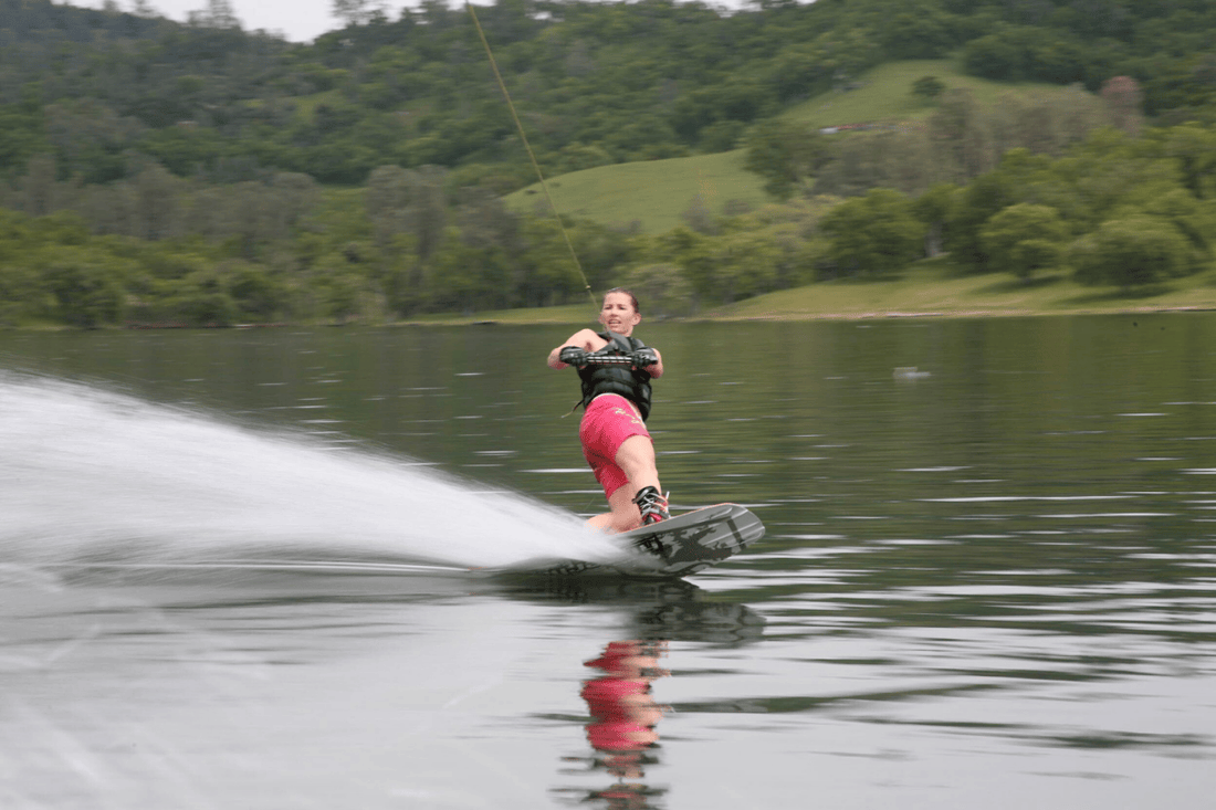 woman on wakeboard being pulled behind a boat on a glass smooth lake. 