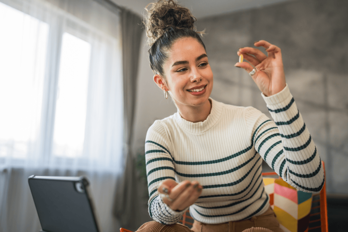 Woman holding up a single vitamin preparing to take her daily vitamins